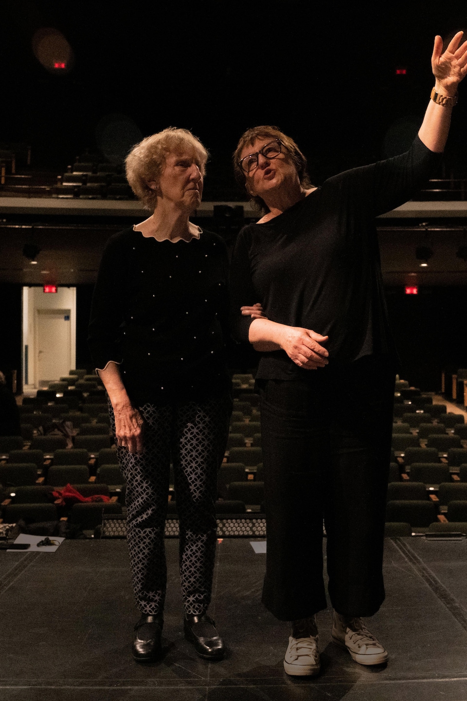 Deux femmes sont sur la scène d'un théâtre bras dessus bras dessous. 
