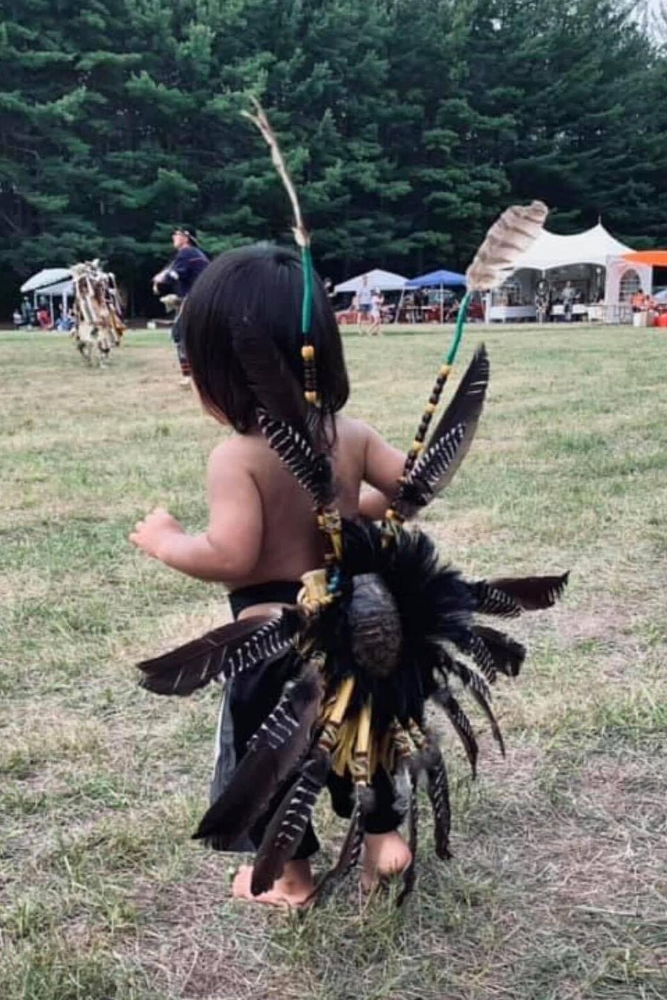 Un enfant de dos avec une regalia faite de plumes et de carapace de tortue.