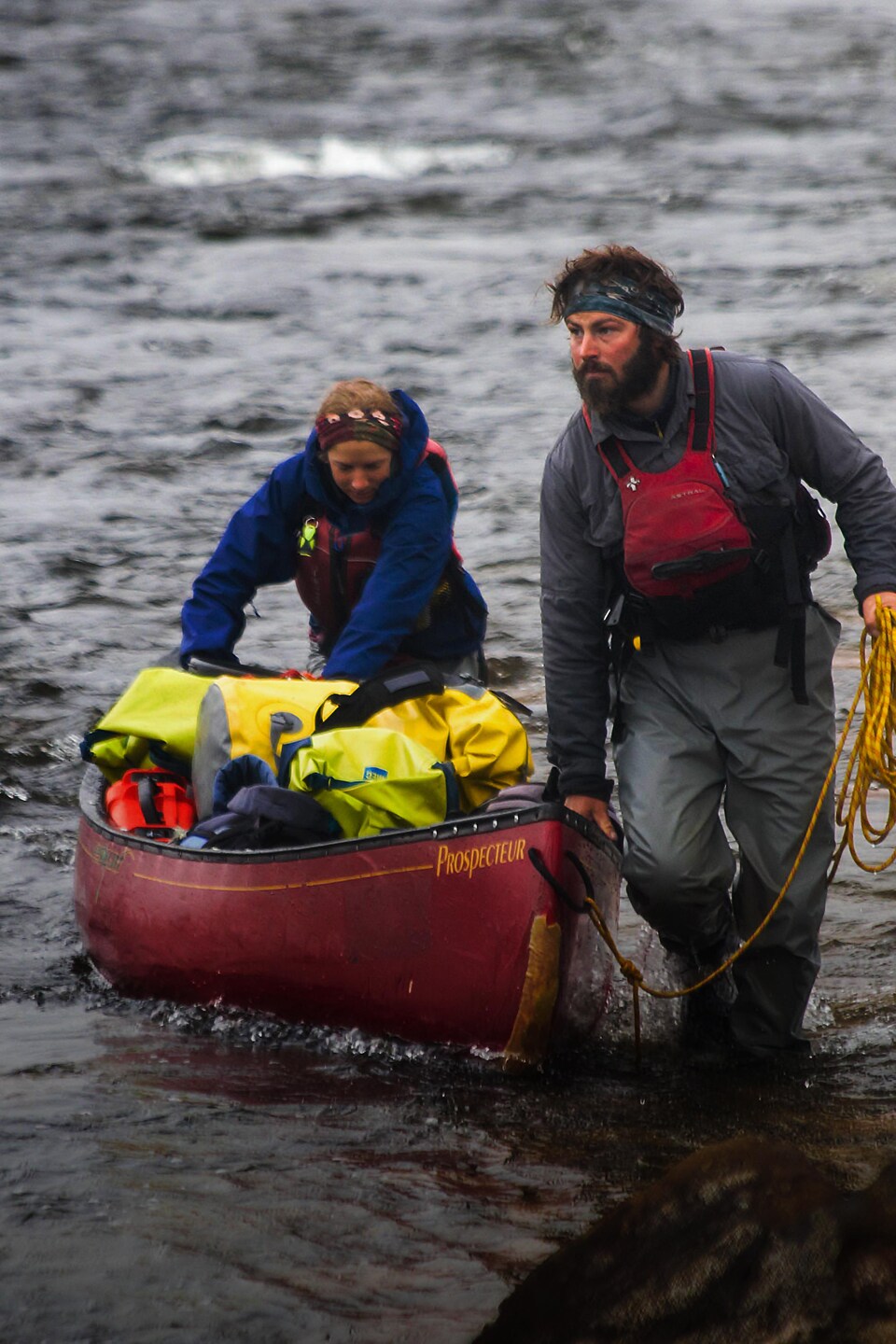 Un des aventuriers, accompagné par sa copine, pousse un canot en bordure de rivière.