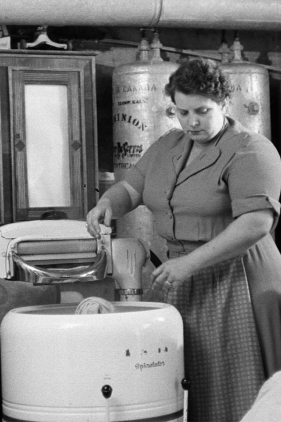 Une femme lave des draps dans une machine à laver semi-automatique à essorage manuel. 