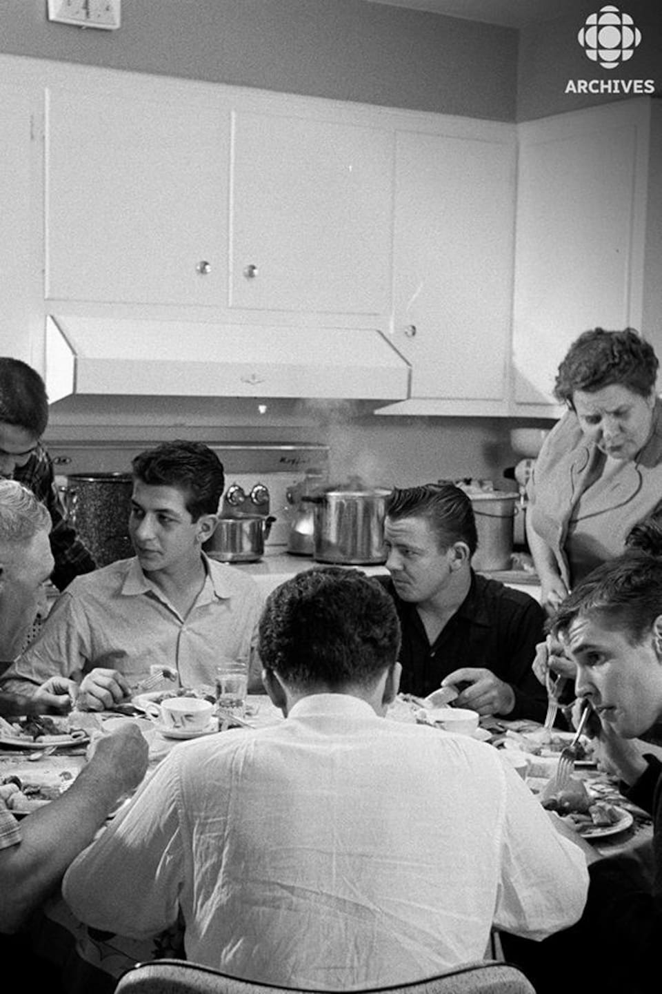 Une famille nombreuse mange autour d'une table ronde dans une cuisine. 