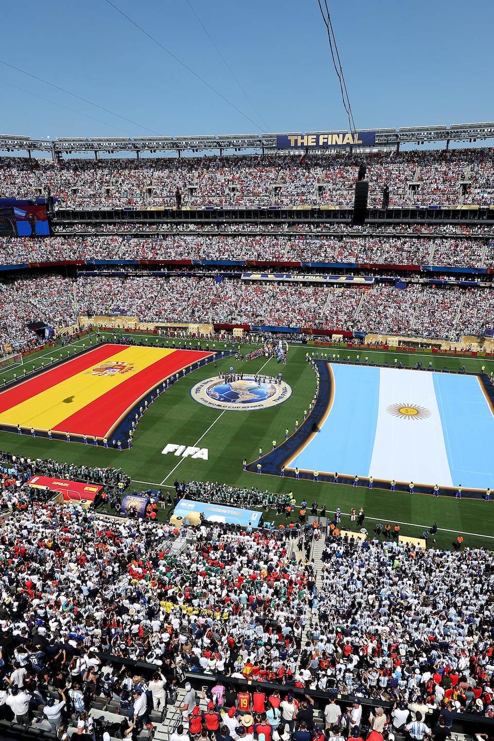 Des estrades sont bondées alors que deux immenses drapeaux de l'Espagne et de l'Argentine sont déployés sur le terrain de soccer, entourés des joueurs des équipes respectives.