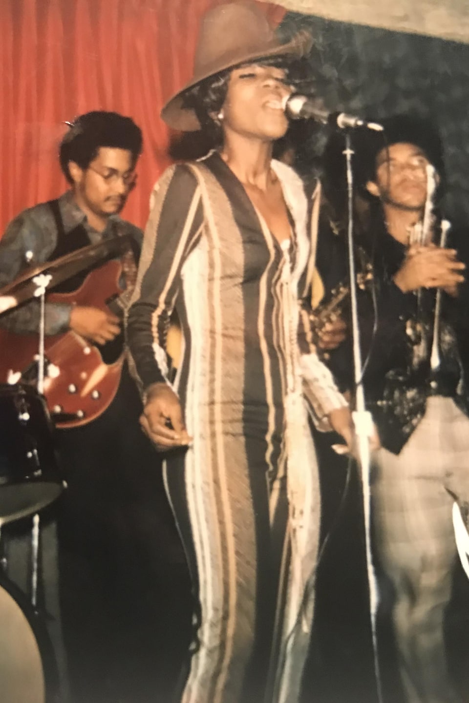 Une femme chante sur une scène avec, derrière elle, deux musiciens.