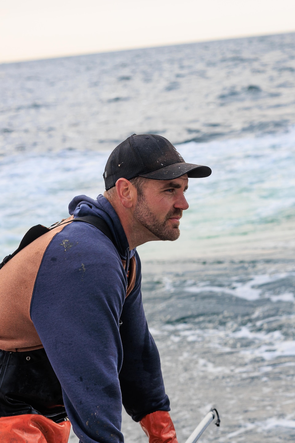 Un homme tient un crocher sur bateau dans une mer houleuse.