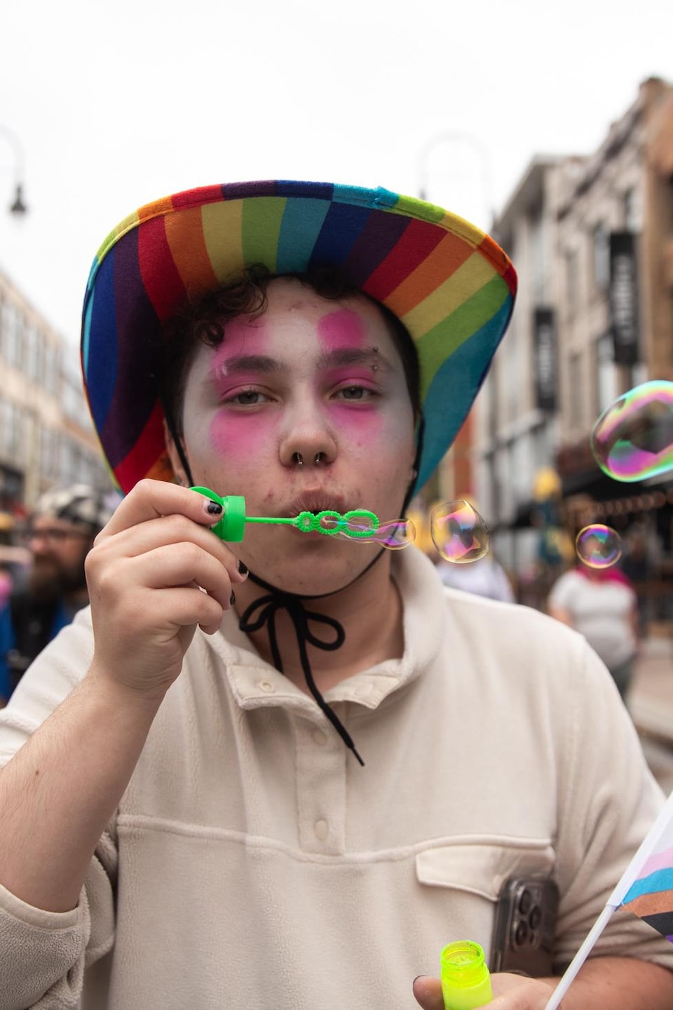 Une personne vêtue d'un chapeau aux couleurs de la communauté LGBTQ+ souffle des bulles. 