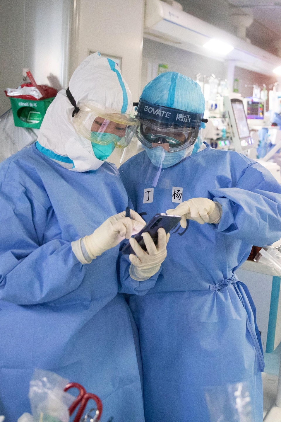 Deux membres d’une équipe médicale en tenue de protection examinent un téléphone.