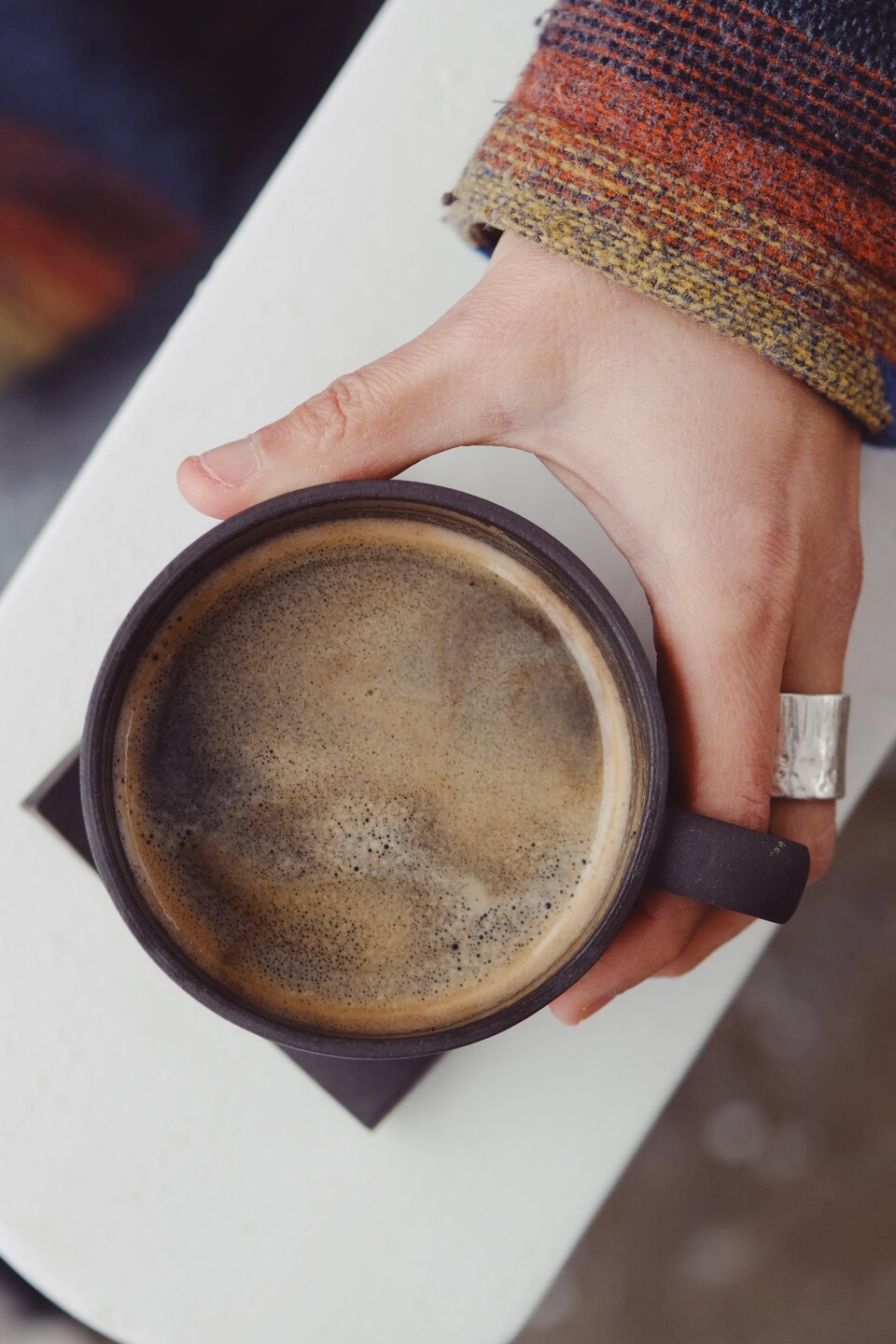 La main de Mélanie Gagné qui tient une tasse de café. Il y a un peu de mousse sur le dessus.