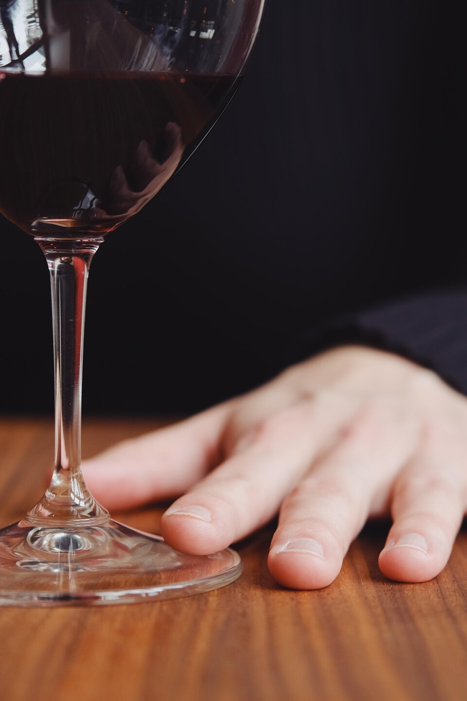 La main de Caroline Beaulieu en gros plan. Son index est délicatement déposé sur le pied de la coupe de vin.