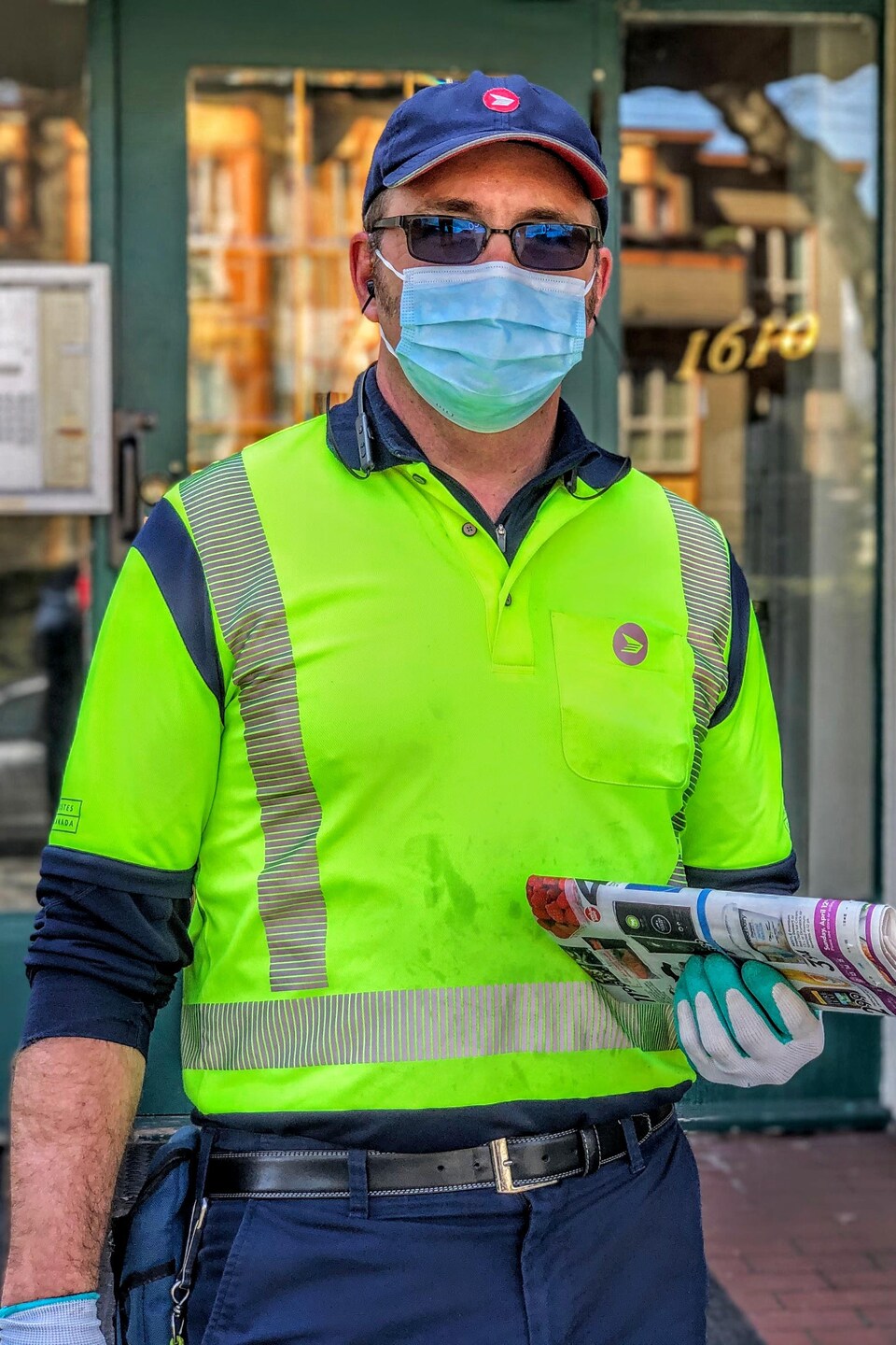 Tony Albertson portant un masque, tenant des circulaires, devant un immeuble.