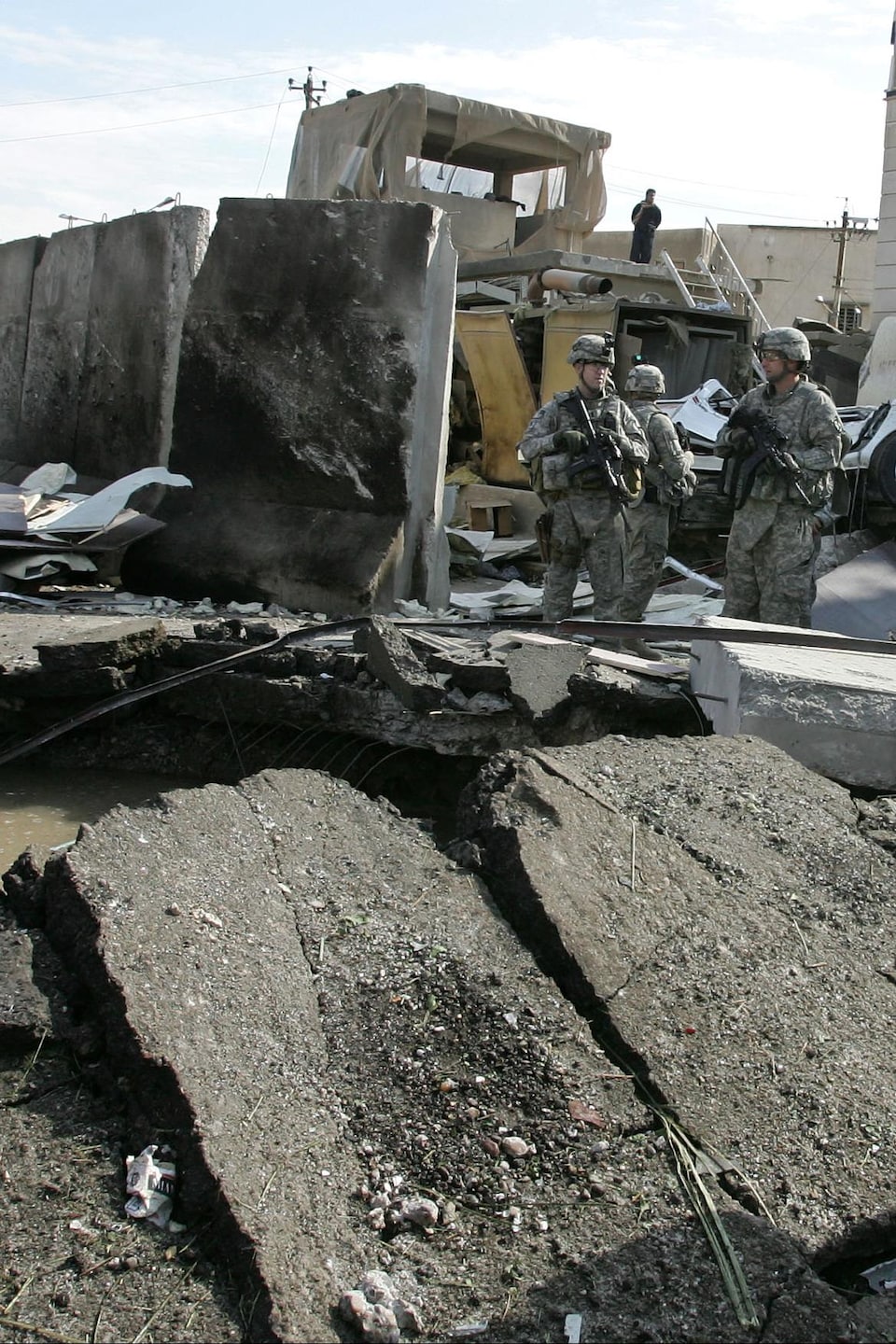 Un militaire se tient près du lieu de l'impact. Le sol est déformé.