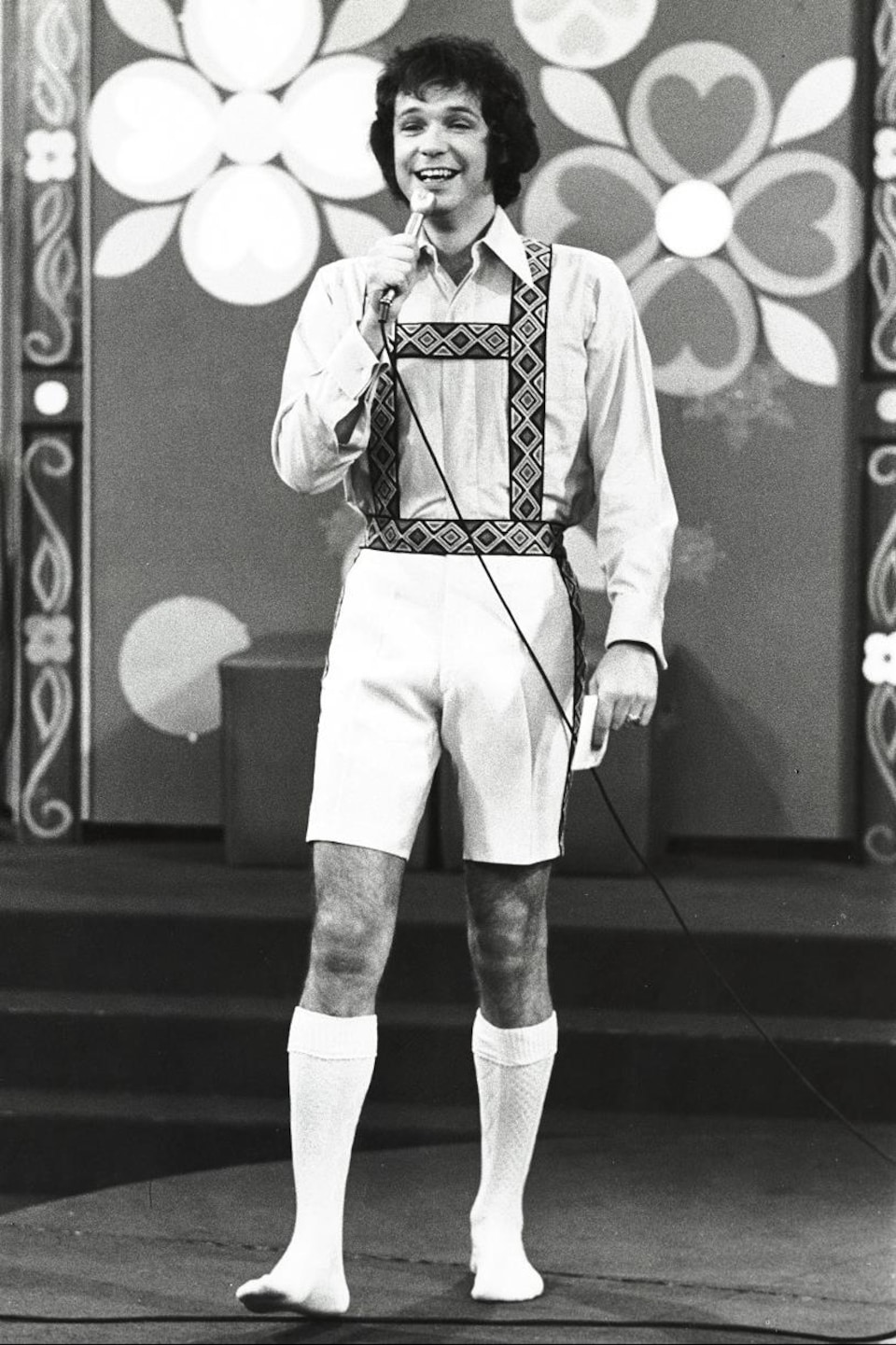 Dans un studio de télévision, Jacques Boulanger en culottes courtes et micro à la main.