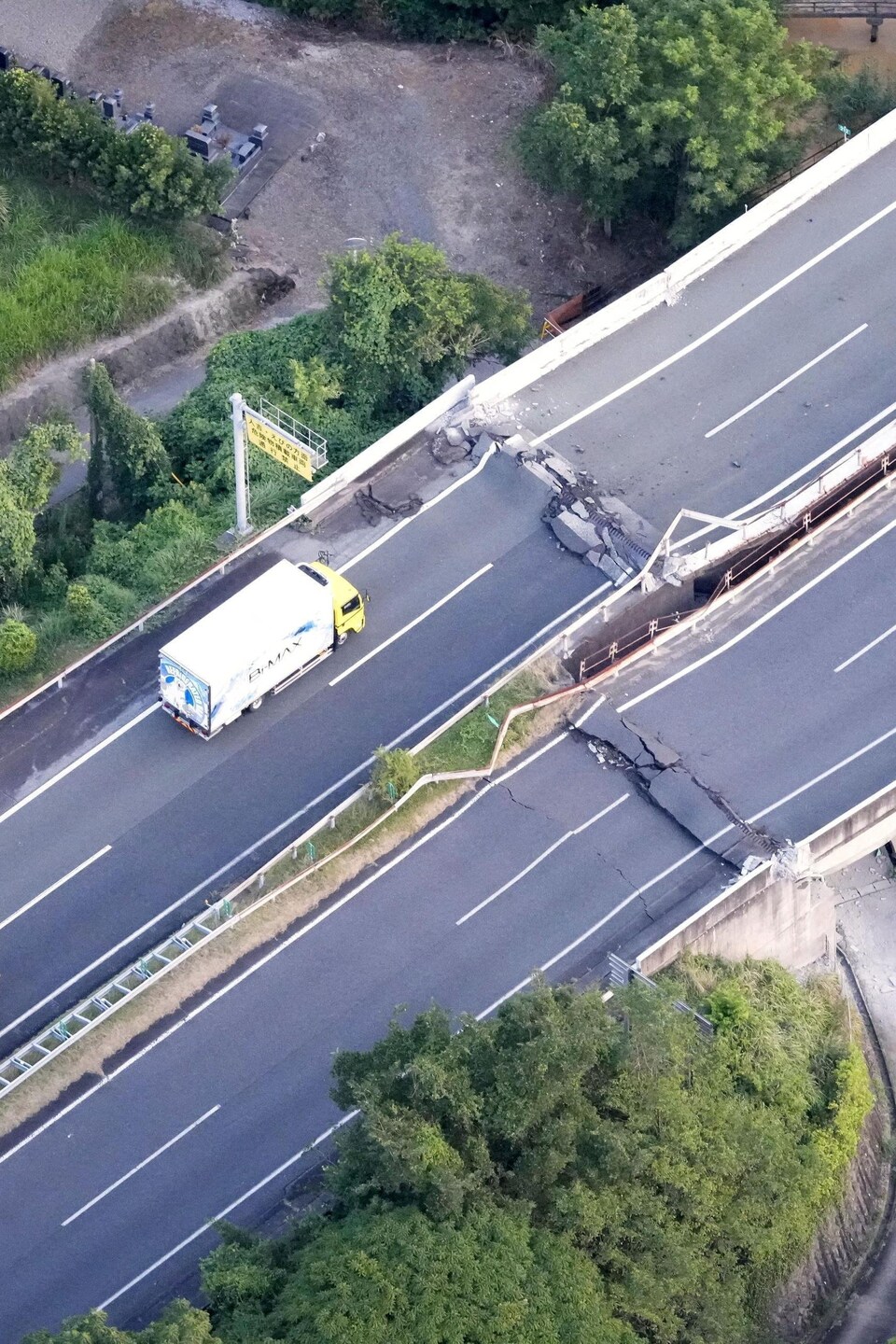 Une autoroute est comme plissée par le tremblement de terre. Des véhicules sont immobilisés devant le pli, qui crée une bosse boquant la circulation.