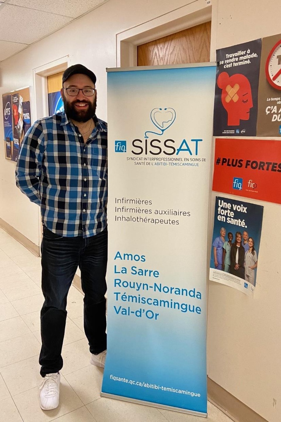 Jean-Sébastien Blais pose à côté d'une affiche de la FIQ-SISSAT.