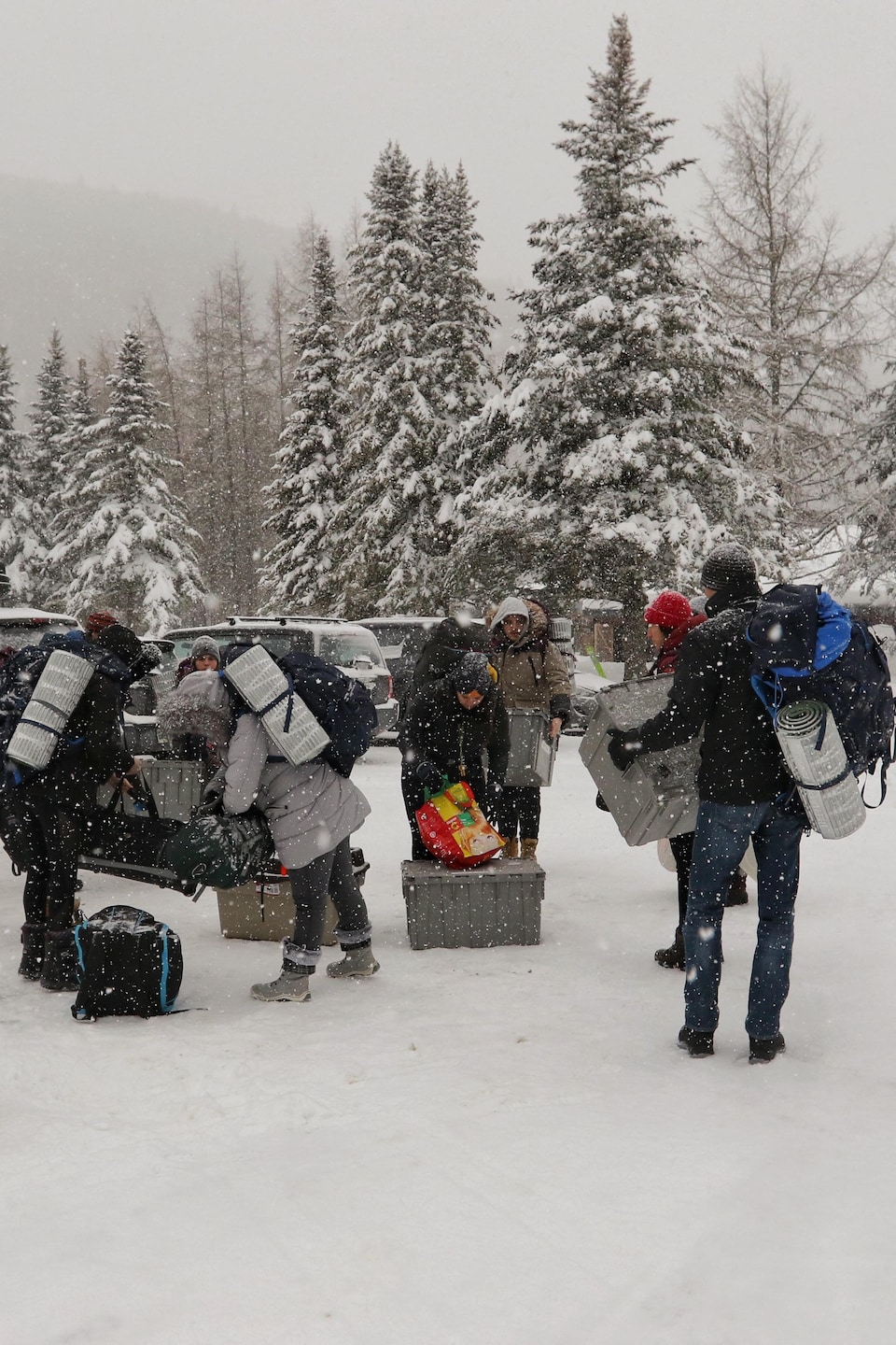 Des jeunes transportent des sacs dos et des boîtes de plastique. Un paysage hivernale les entoure.