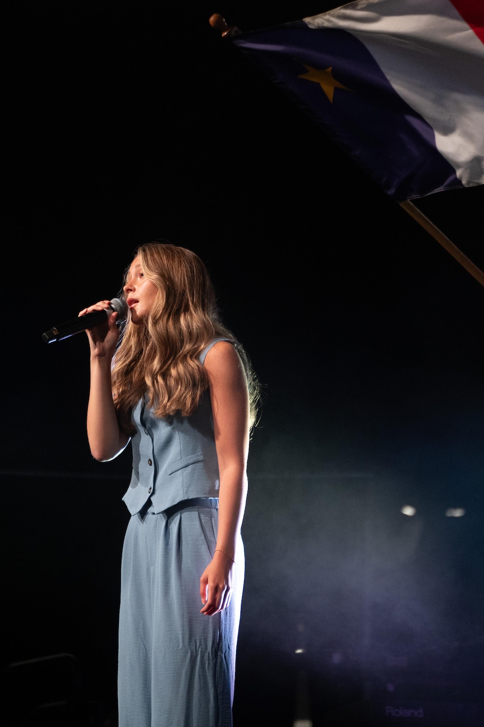 Josiane Comeau chante sur une scène sous un drapeau acadien.
