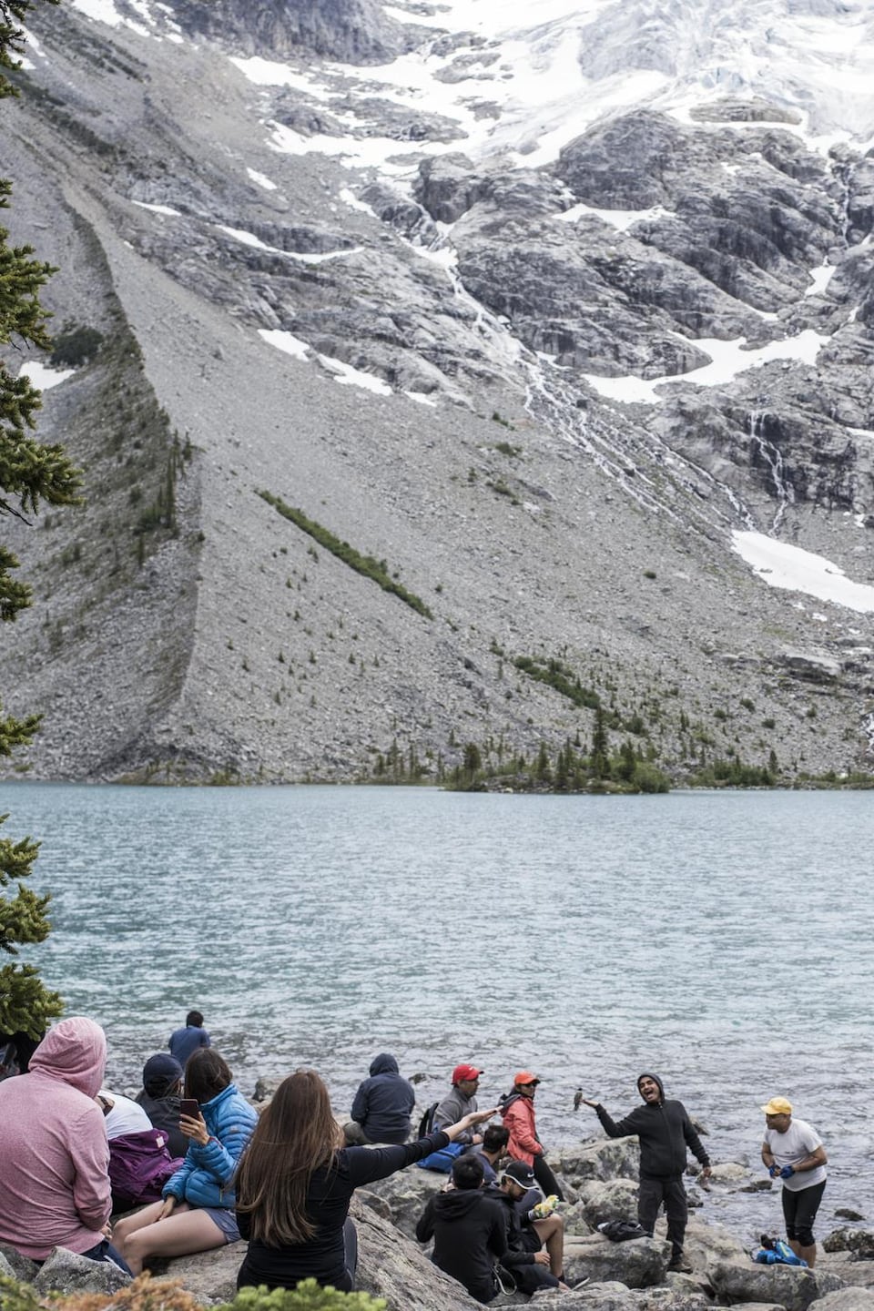 Plusieurs touristes sont assis aux abords d'un lac du parc britanno-colombien Joffre Lakes et se prennent en photos avec des oiseaux.