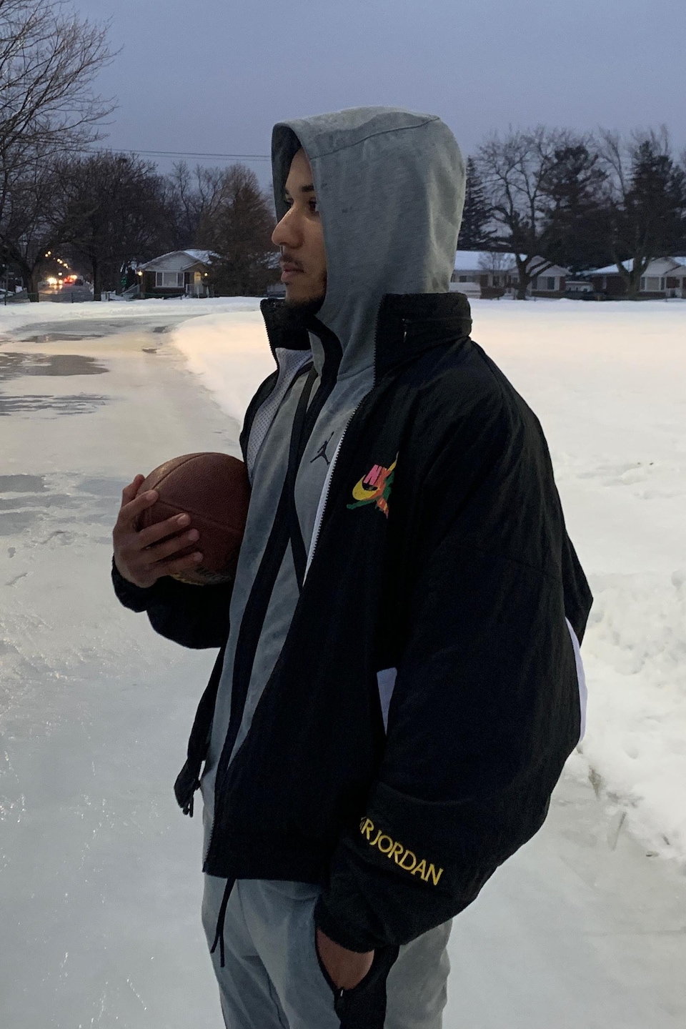 Un jeune homme debout dans un parc l'hiver tient un ballon de football dans ses mains.