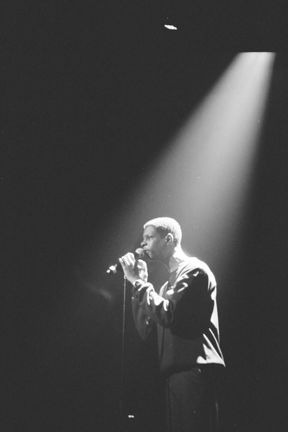 Photo en noir et blanc du chanteur sur la scène, devant un micro.