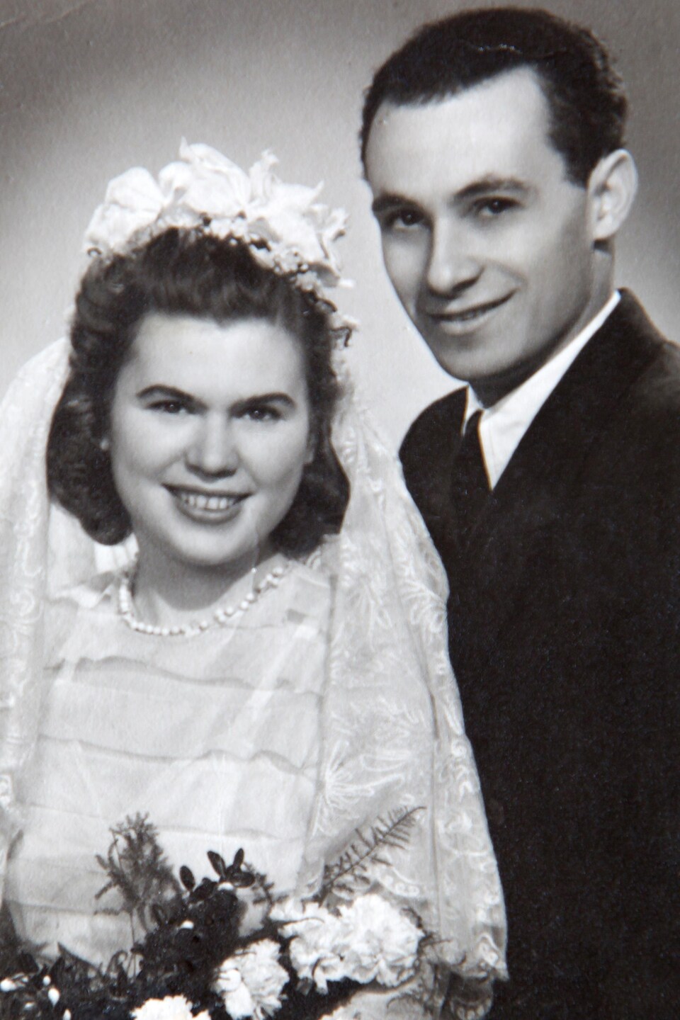 Vera et George sont vêtus de leurs habits de mariage et sourient à la caméra, sur une photo en noir et blanc.
