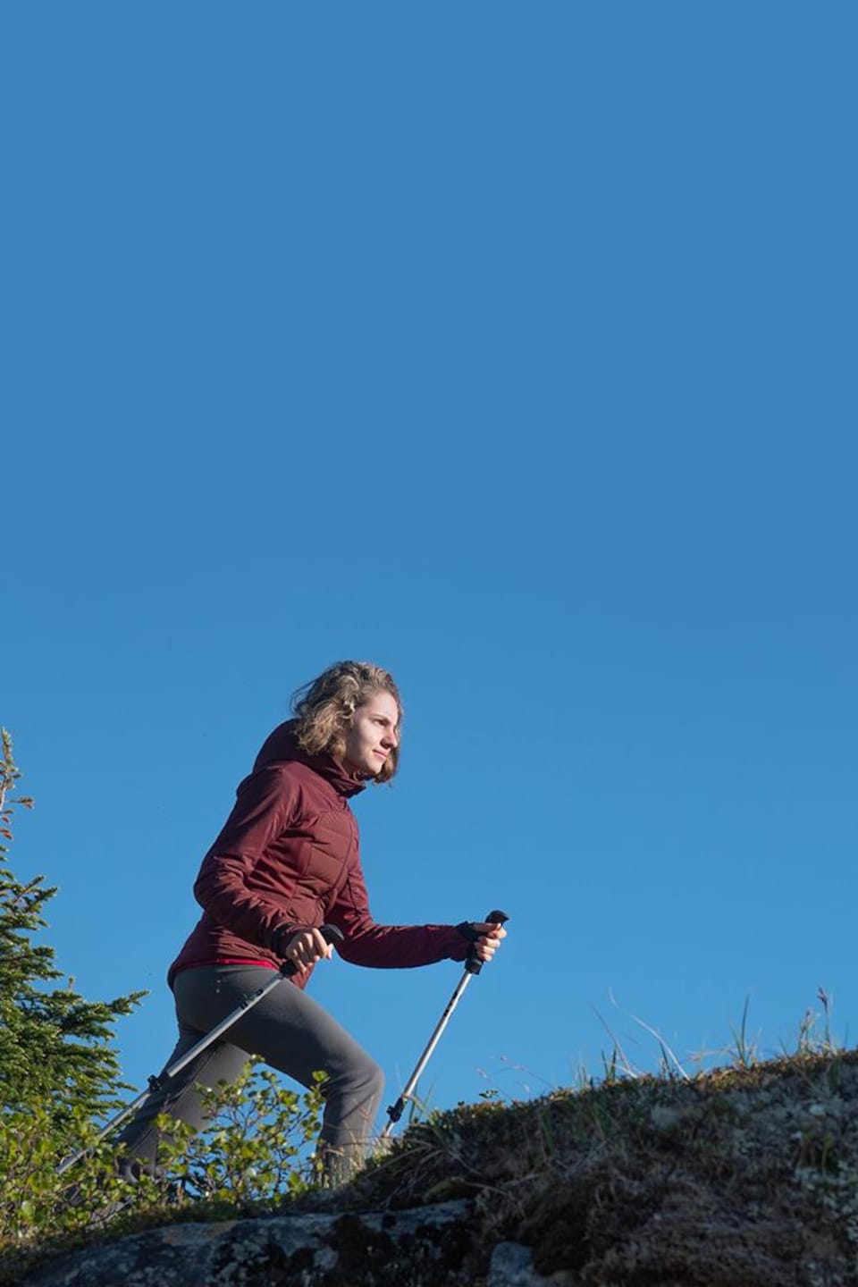 Photographie de Simone, qui marche avec des bâtons de randonnée sur un cap rocheux et montagneux.