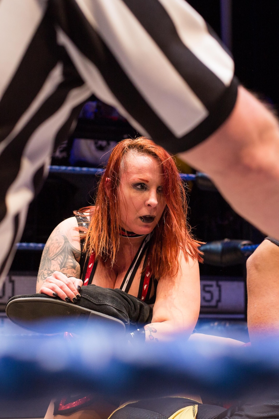 Au milieu du ring, la lutteuse LuFisto coince le pied de son adversaire dans ses bras. 