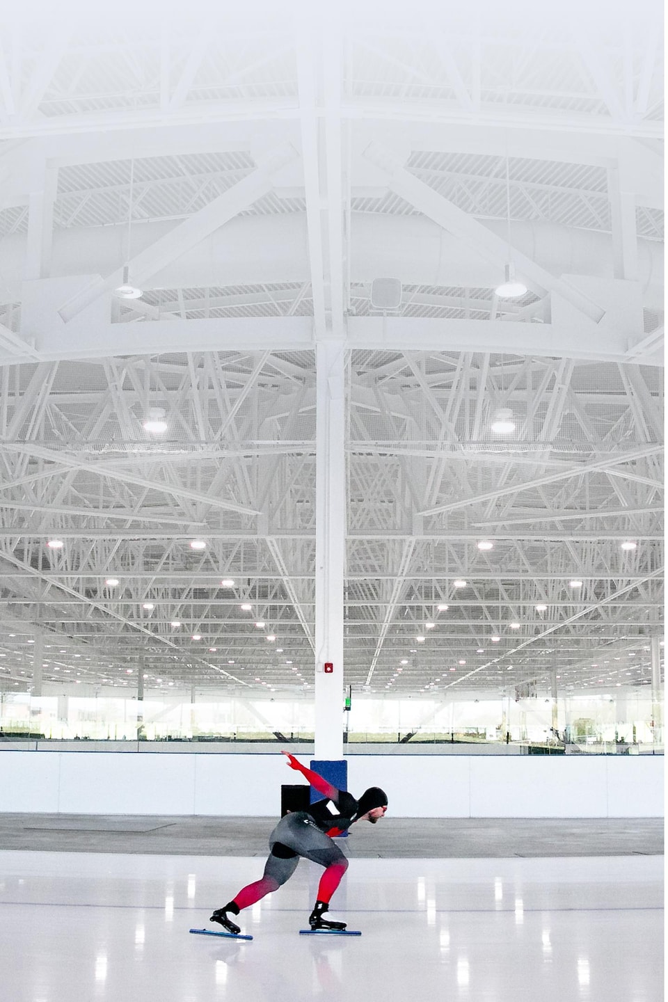 Un homme en habit de patineur de vitesse s'élance sur un anneau de glace intérieur.