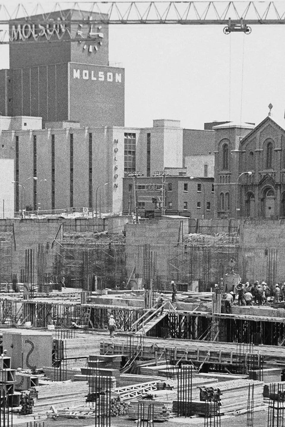 Chantier de construction avec église et usine Molson en arrière plan. 