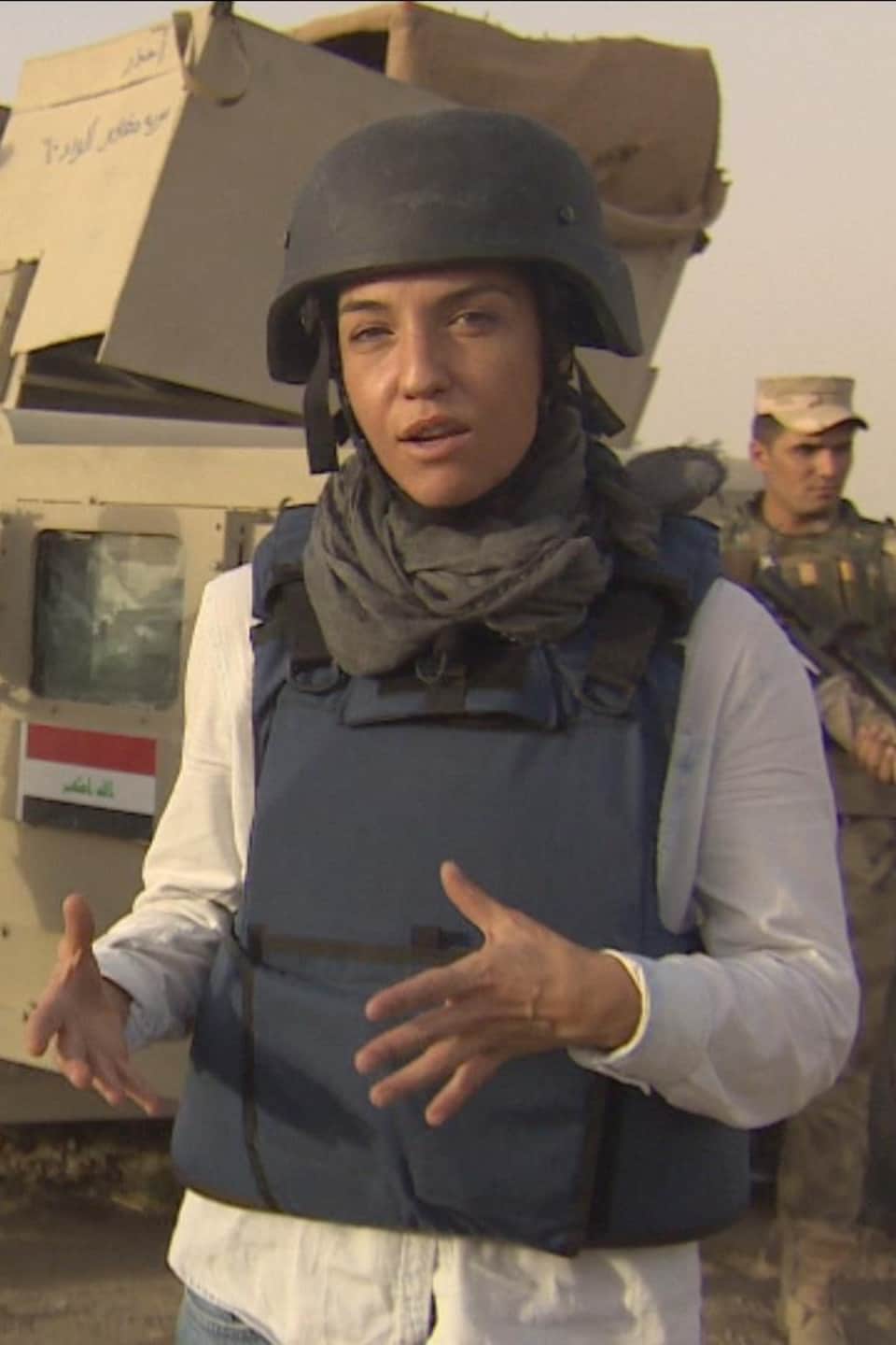 La journaliste Marie-Ève Bédard, portant
casque et gilet pare-balles en Irak avec des militaires irakiens en arrière plan.