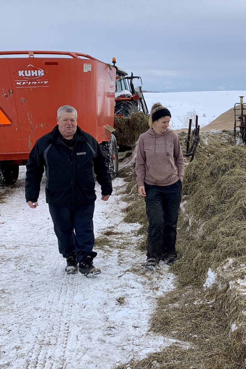 Maurice et Geneviève Migneault marchent près des vaches qui mangent du foin.