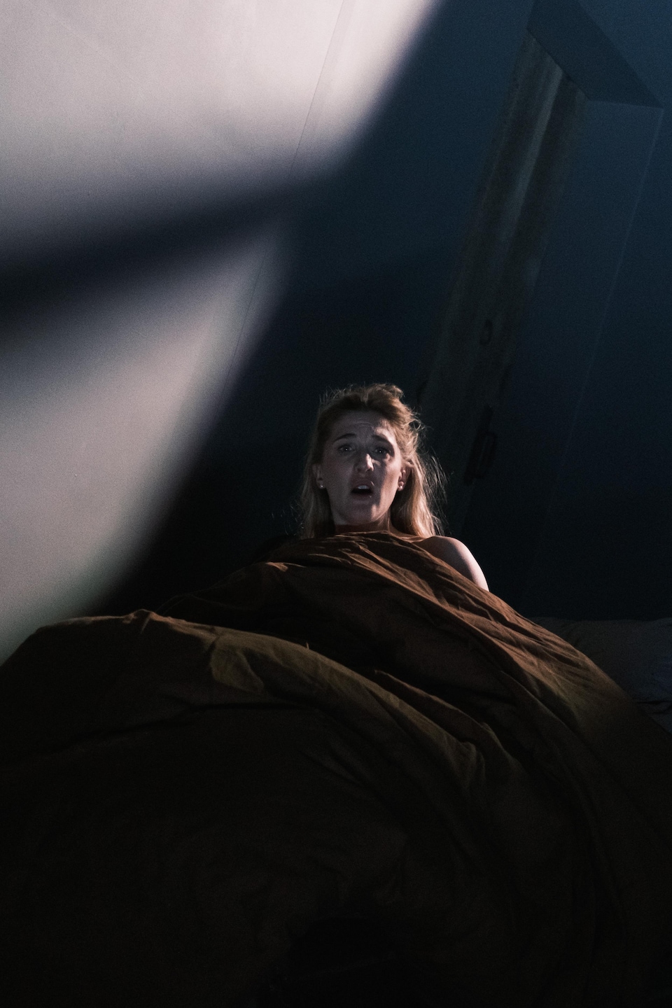 Mylène Mackay se redresse dans un lit, avec une expression inquiète.