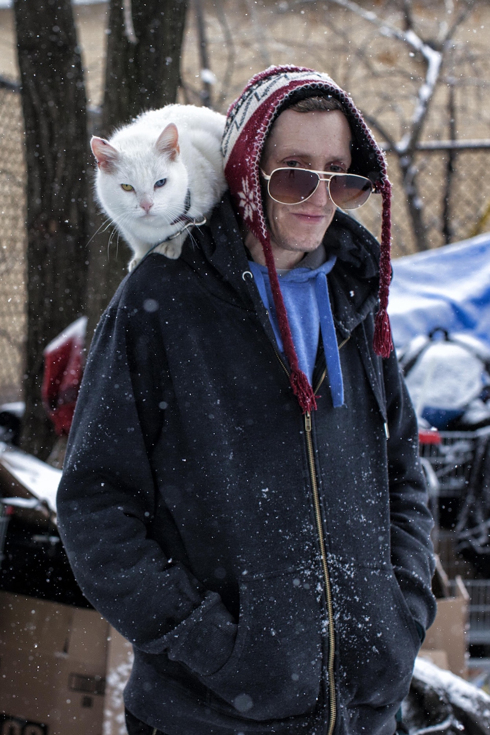 Un homme en situation d'itinérance porte son chat aux yeux vairons sur ses épaules.