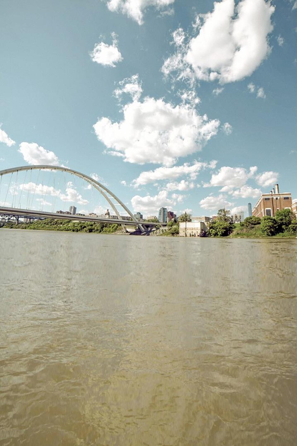 Rivière Saskatchewan Nord en vue large dans la ville d'Edmonton, avec un pont et une ancienne usine au loin.