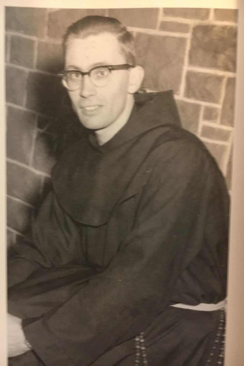 Une photo en noir et blanc montre un jeune Raymond Currie en soutane, en 1960.