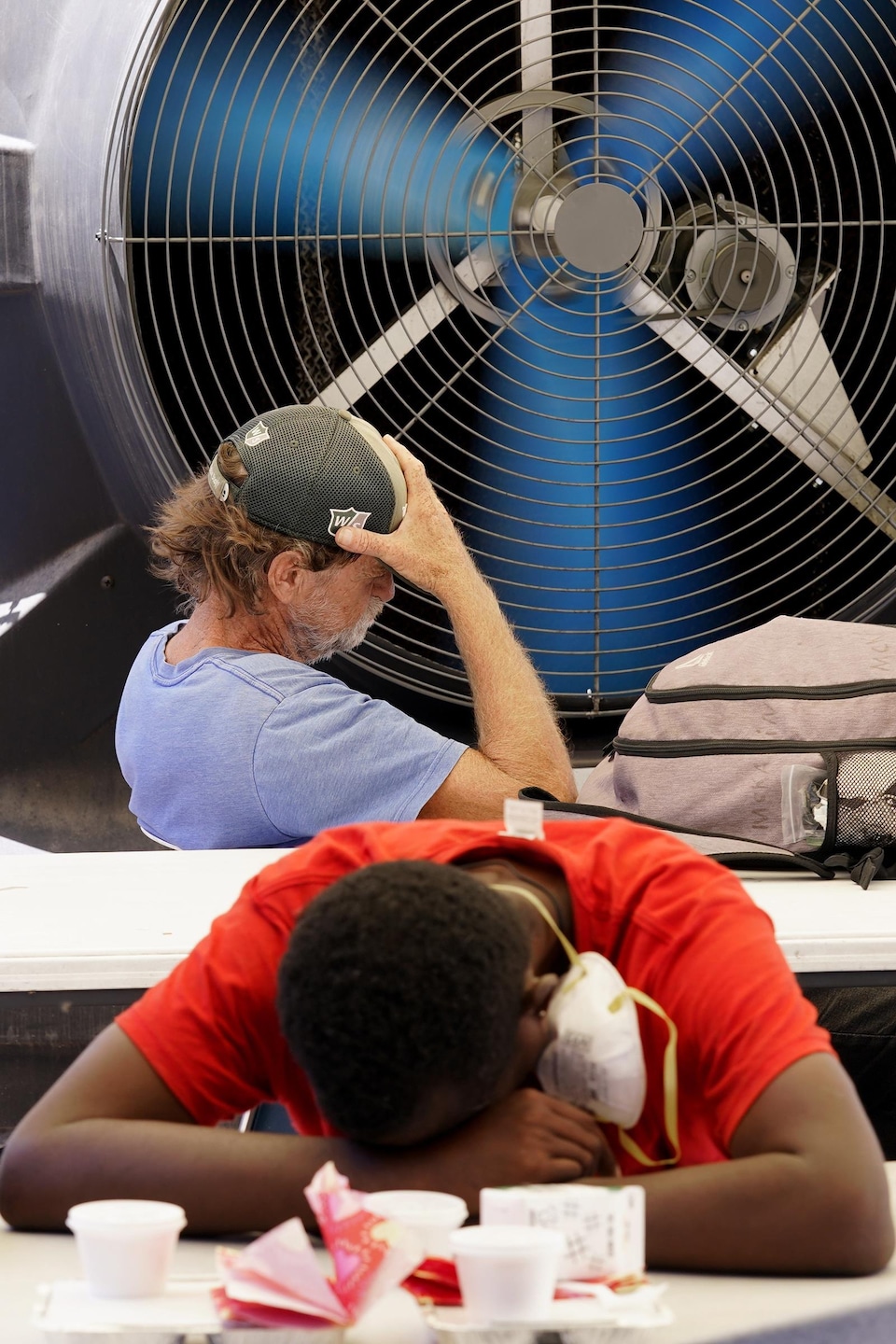 Deux personnes assises devant un immense ventilateur.