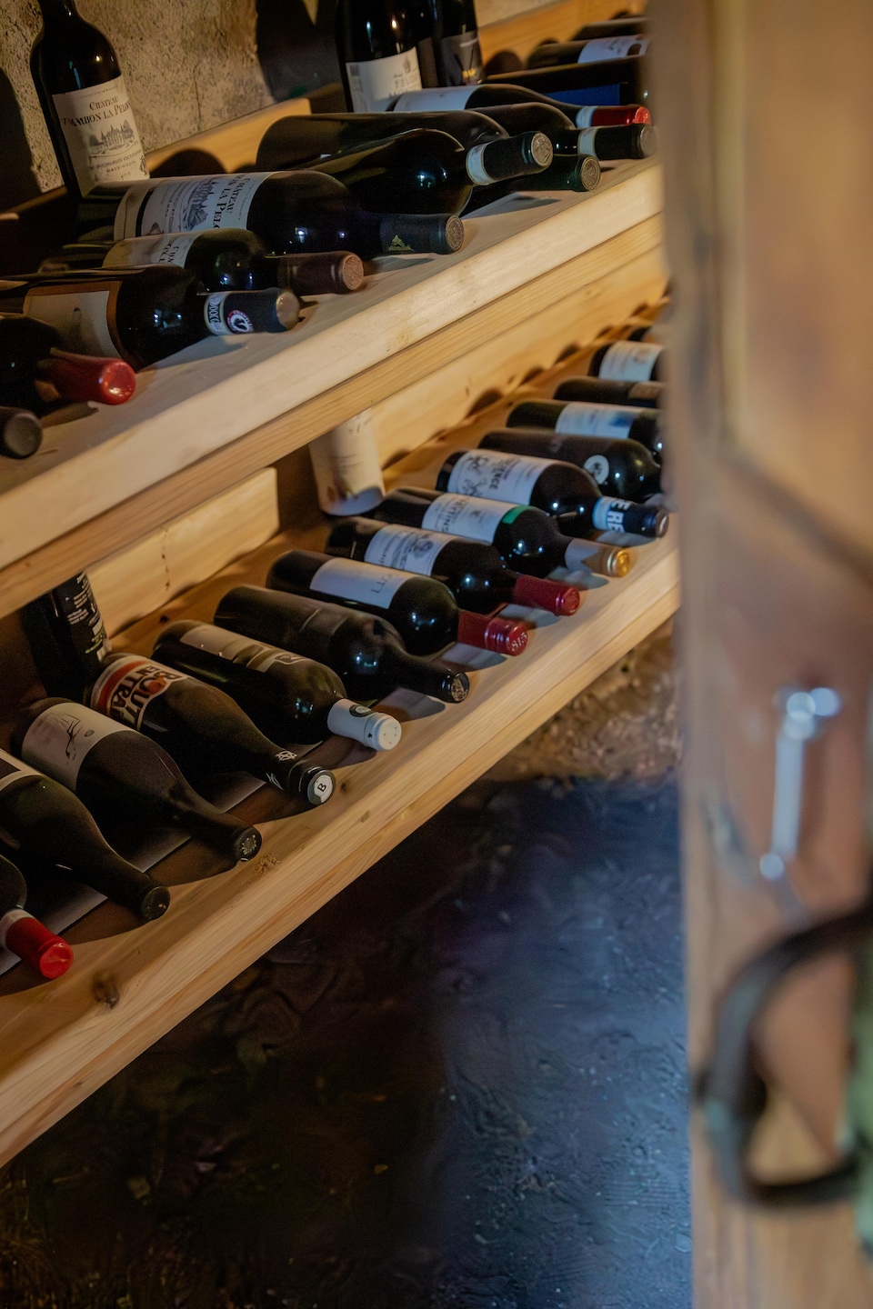 Une porte en bois entrouverte sur des étagères contenant plusieurs bouteilles de vin rouge.