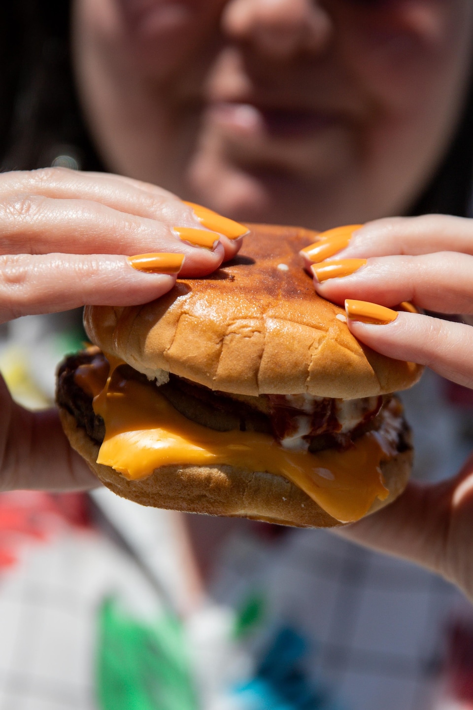Une personne tient à deux mains un hamburger garni de fromage fondu.