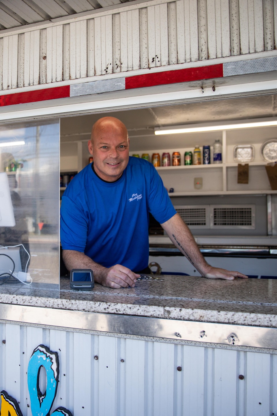 Un homme souriant en t-shirt bleu se tient au guichet de la cantine Chez Michelin.