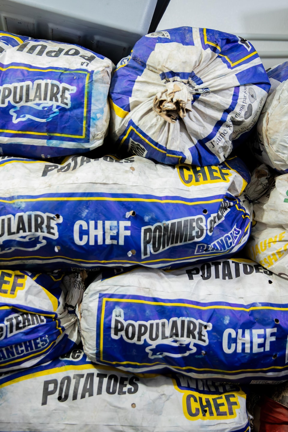 Des sacs de pommes de terre de marque « La Populaire » sont empilés dans une réserve.
