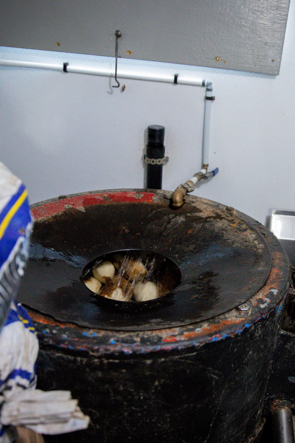 Des pommes de terre tournent sous un jet d'eau dans une éplucheuse industrielle, à côté de sacs de pommes de terre.