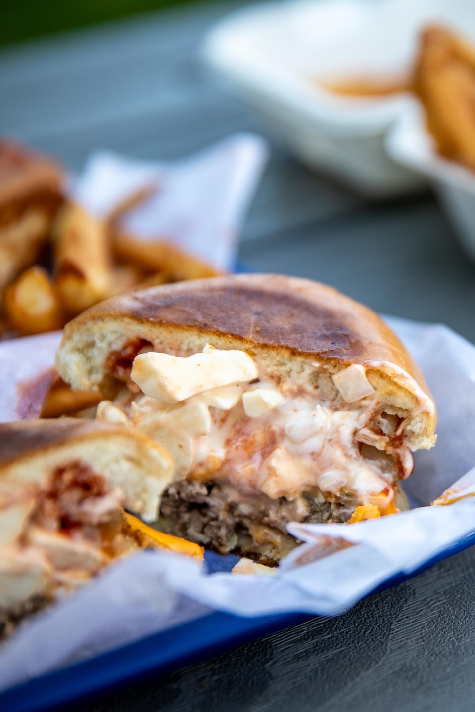 Un burger coupé en deux garni de fromage et de sauce repose sur un plateau, à côté d'un contenant de frites.