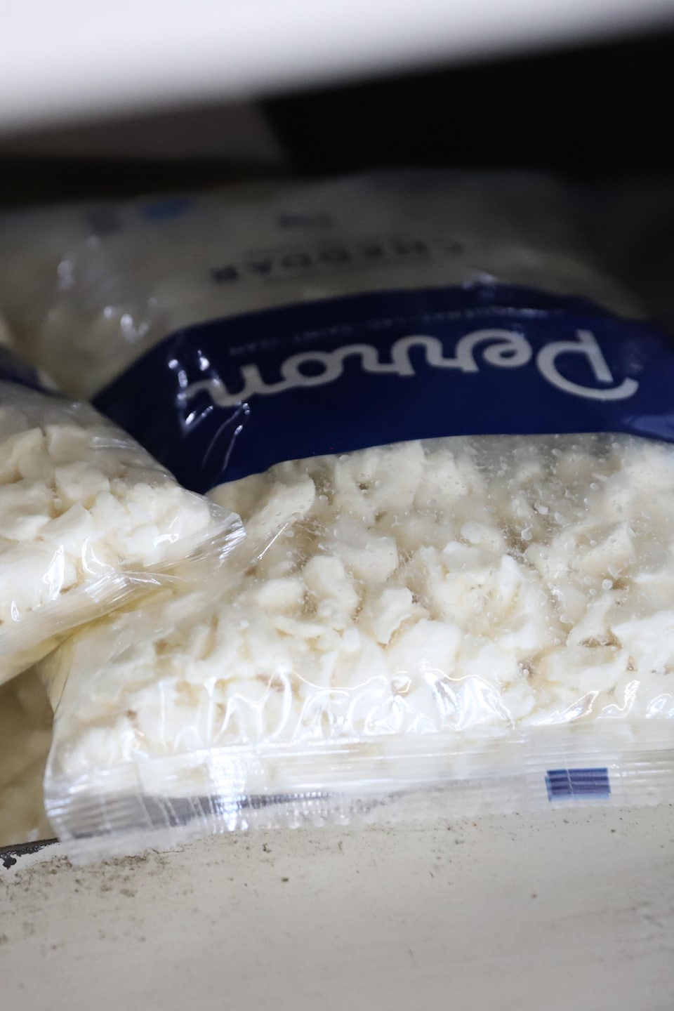 Des sacs de fromage en grain de la Fromagerie Perron sont empilés sur une étagère.