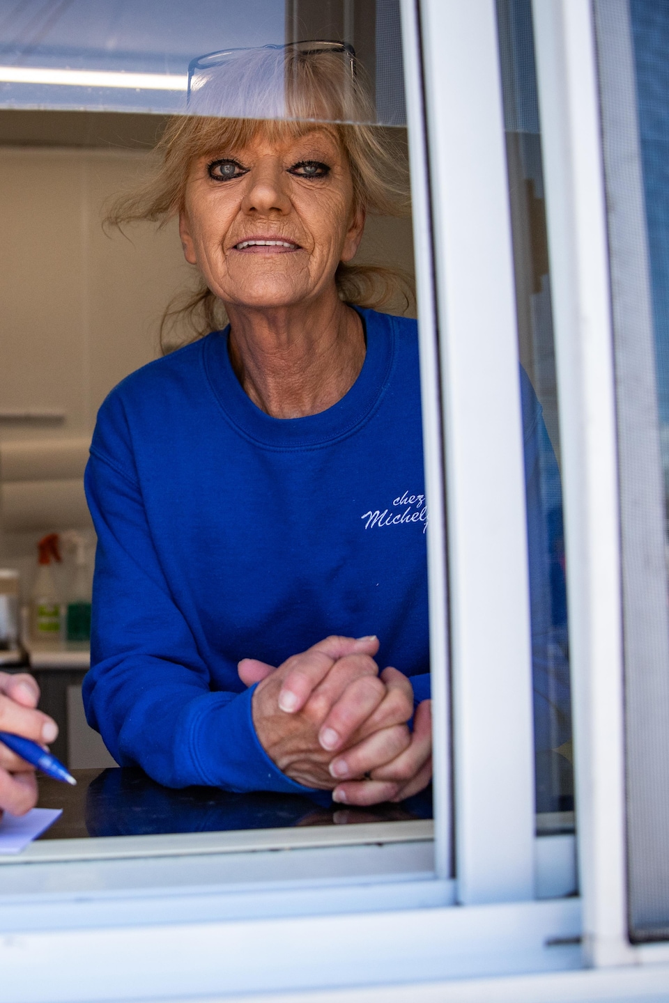 Deux employées en chandail bleu de la cantine Chez Michelin sourient derrière la fenêtre du comptoir.