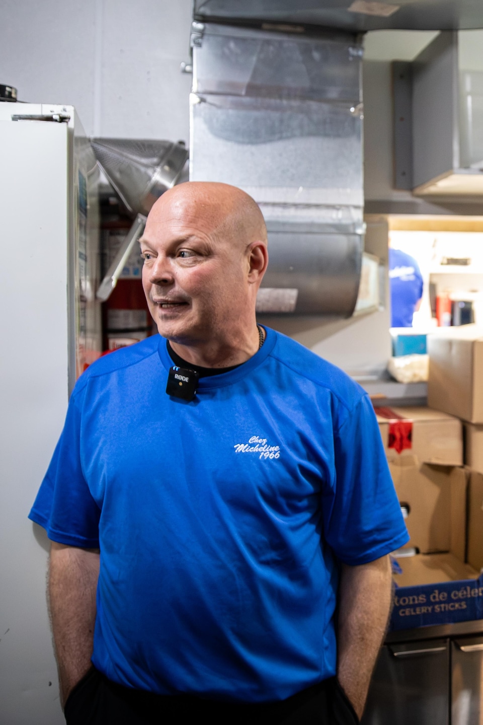 Un homme en t-shirt bleu « Chez Micheline 1966 » se tient debout dans la cuisine du casse-croûte.