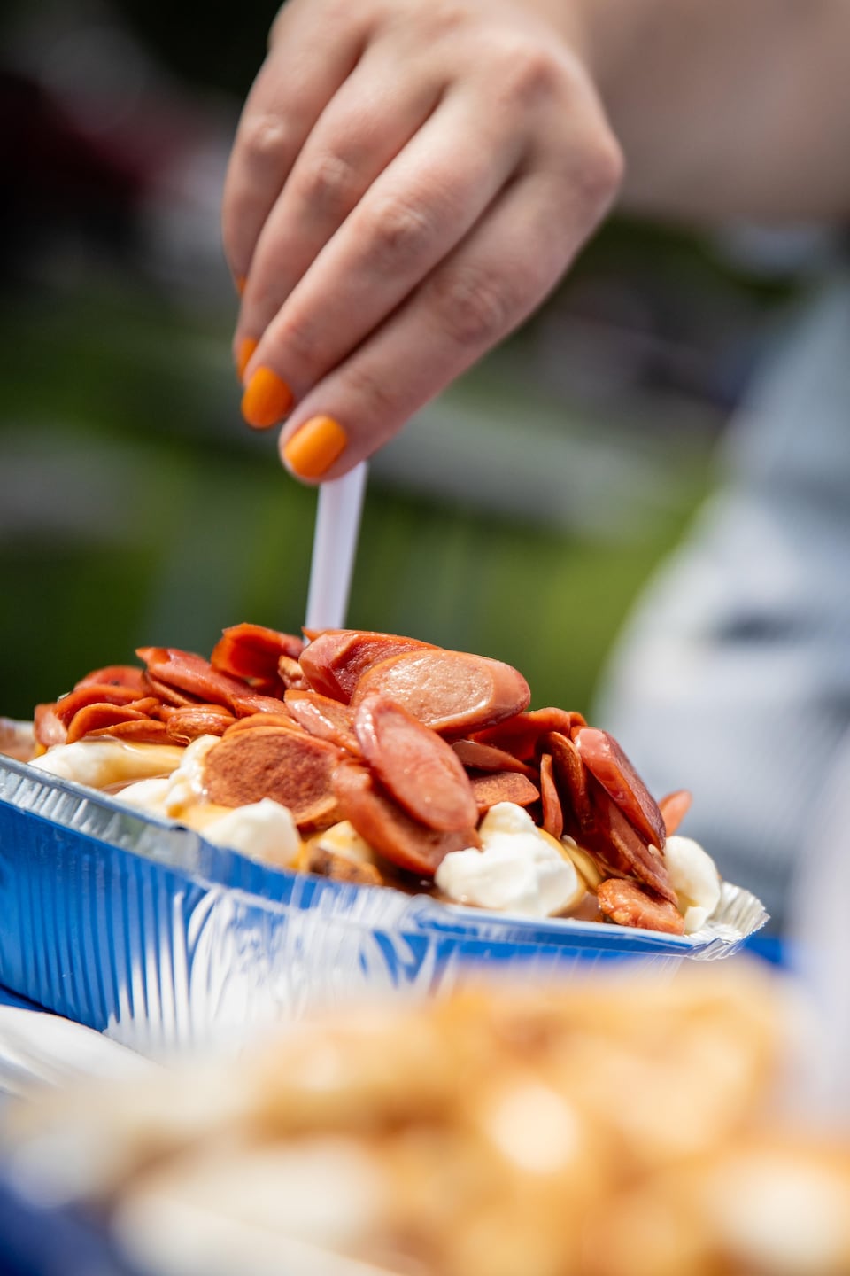 Une personne plante une fourchette dans une poutine garnie de saucisses servie sur un plateau bleu.