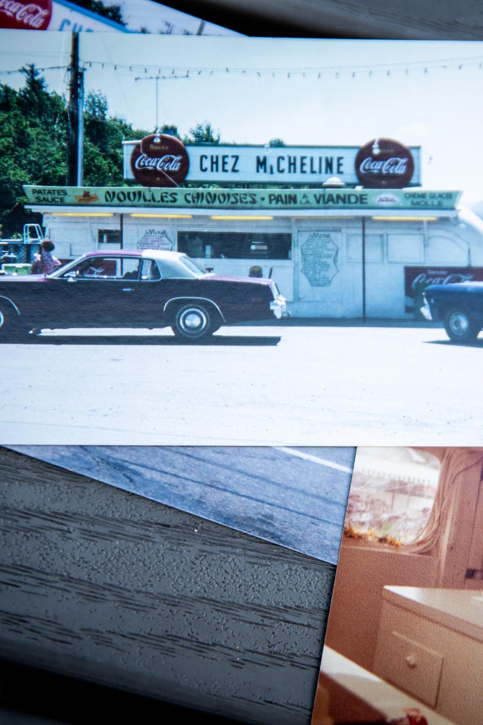 Des photographies imprimées posées sur une table montrent le commerce « Chez Micheline » et une personne auprès d'un enfant en chaise.