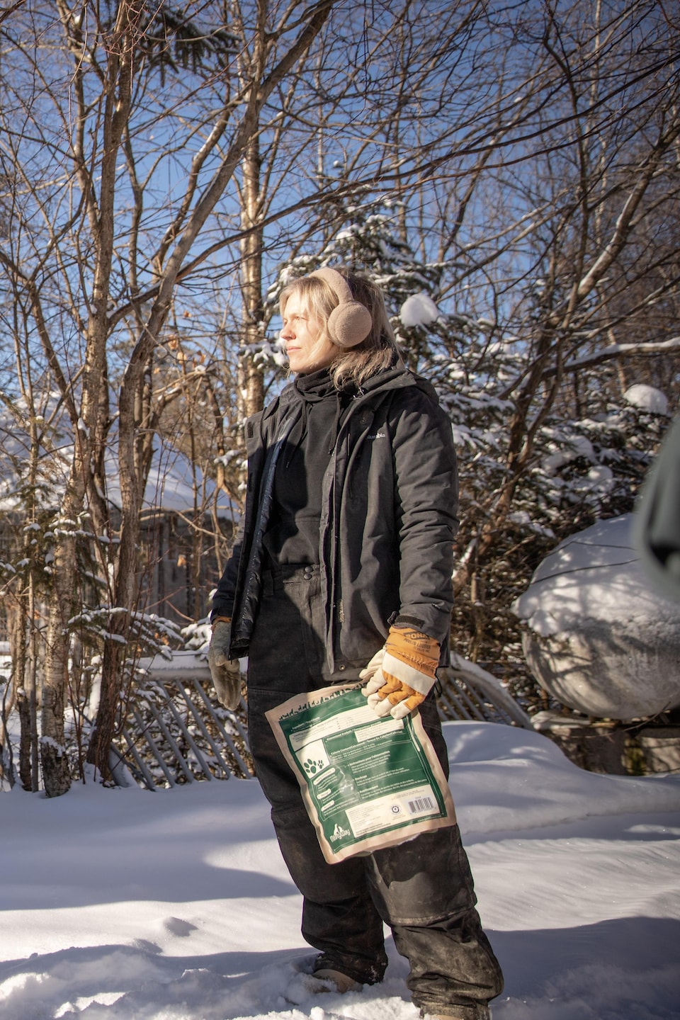 Un homme en vêtements d'hiver et une femme tenant un sac de nourriture discutent dans la neige à côté d'un véhicule utilitaire sport.