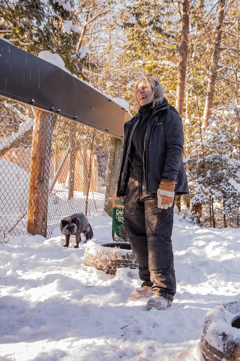 Justine sourit dans un enclos enneigé près d'un renard et de pneus servant aux enrichissements.