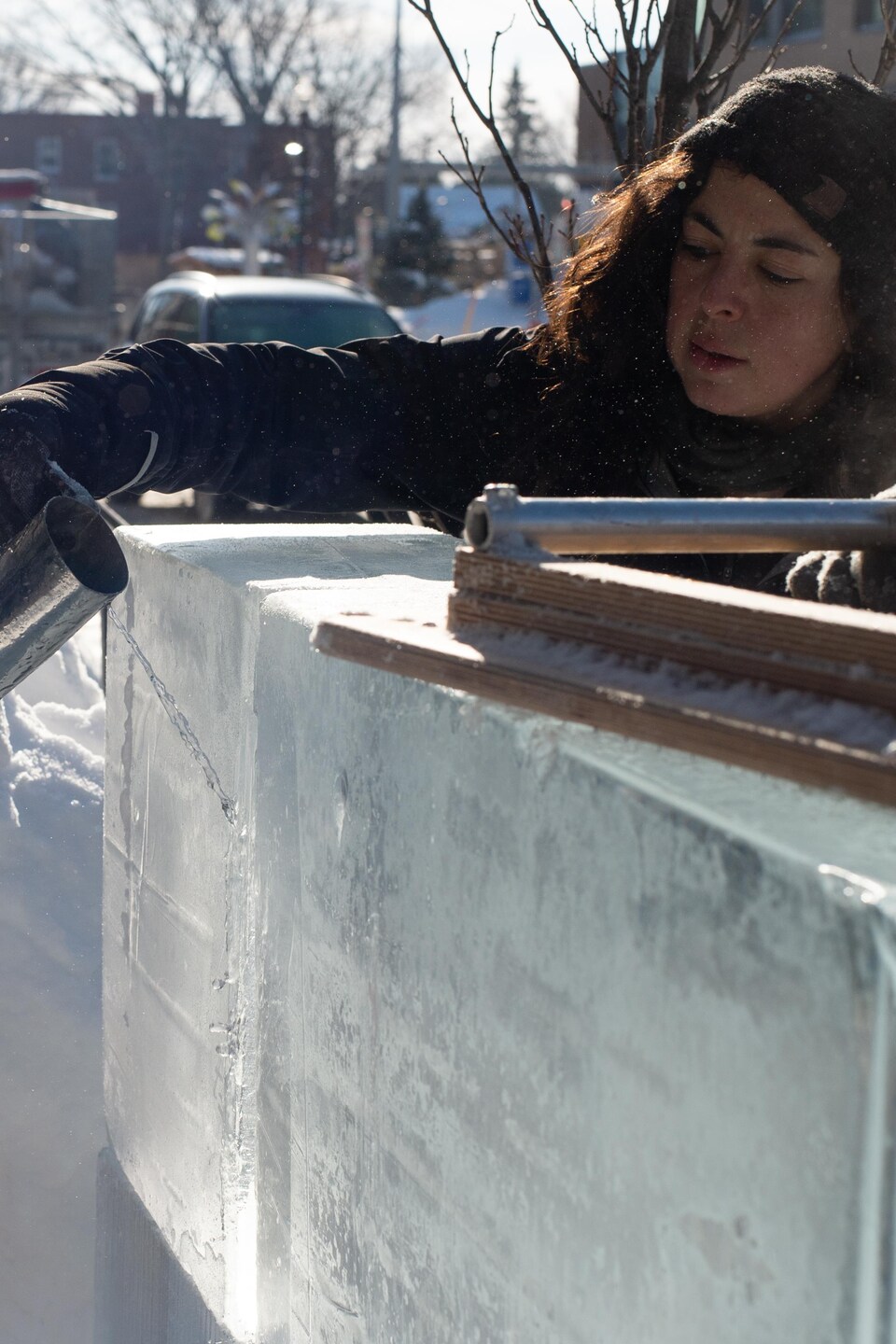 L'artiste, à l'aide d'une petite cruche en métal, verse de l'eau dans une fissure qui se trouve entre deux blocs de glace.