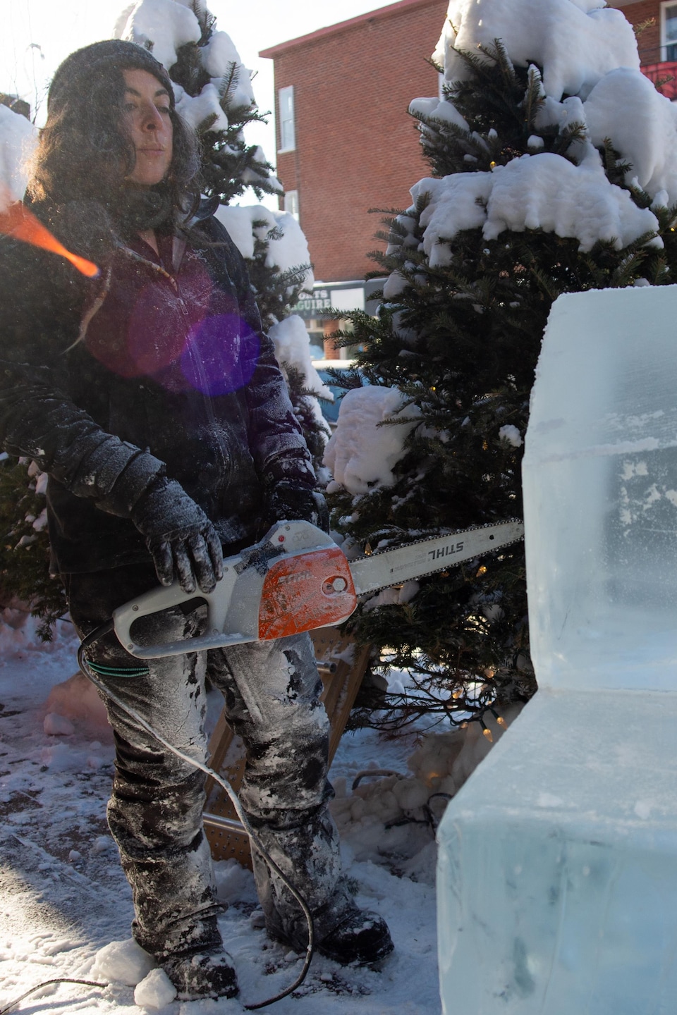 Isabelle se tient debout, avec la scie à chaîne dans les mains, devant la structure de glace. Elle analyse la forme des blocs.