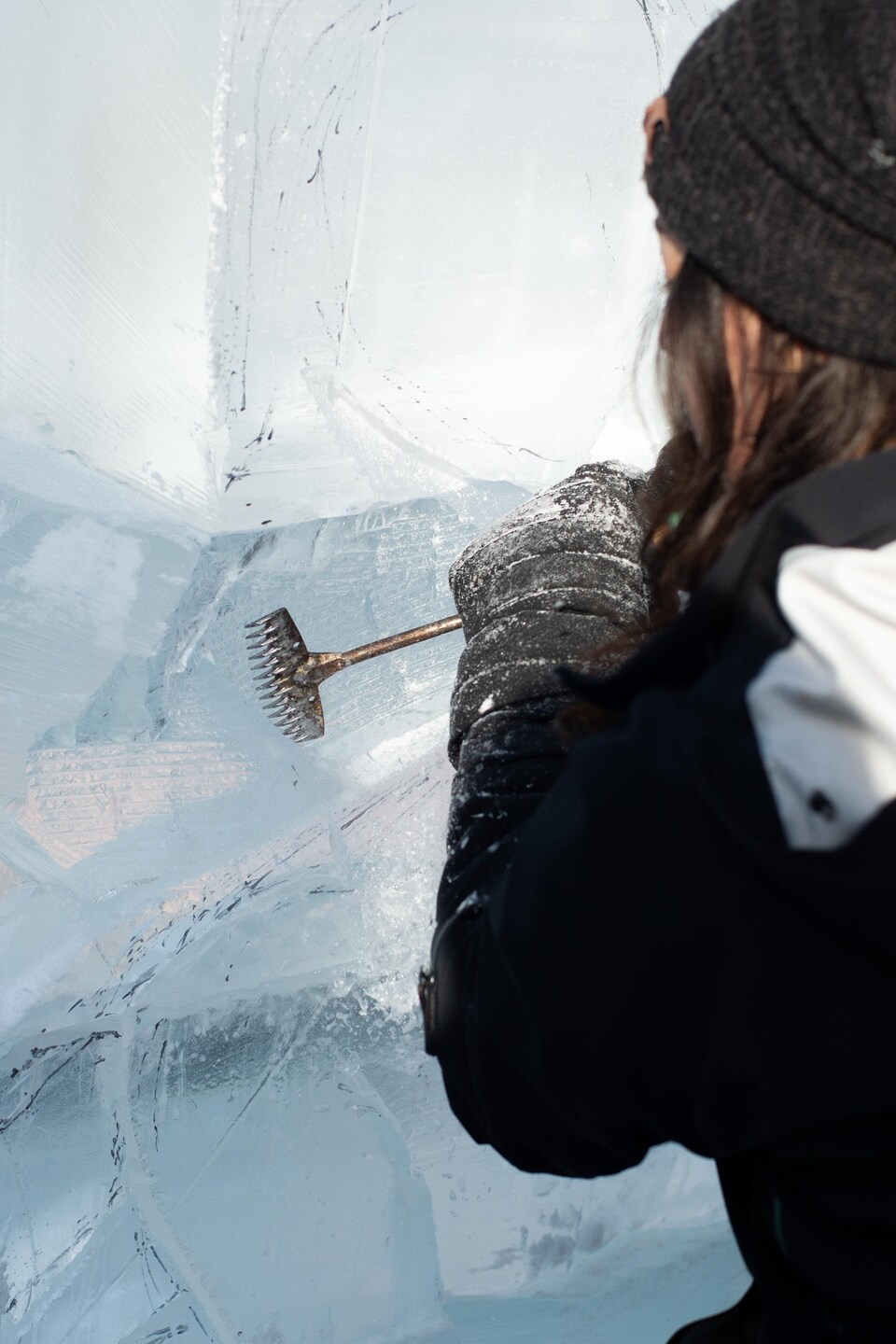 L'artiste, de dos, gratte la surface de la glace à l'aide d'un rasoir sur un manche. L'outil laisse une texture achurée sur la glace.